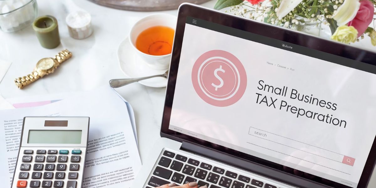 A laptop showing "Small Business Tax Preparation" next to a calculator and a cup of tea.