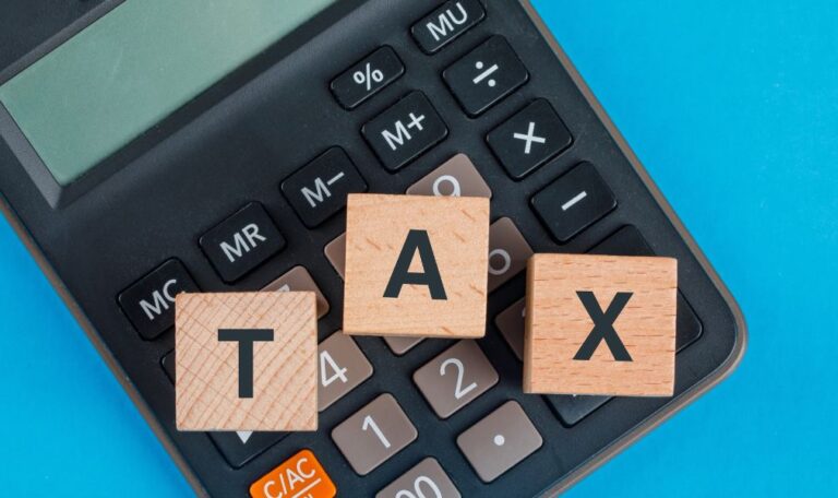 A calculator on a blue background with wooden blocks spelling "TAX" on top of the keys.
