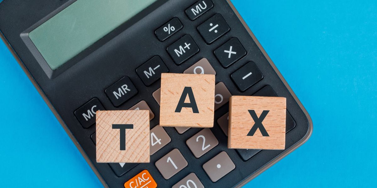 A calculator on a blue background with wooden blocks spelling "TAX" on top of the keys.